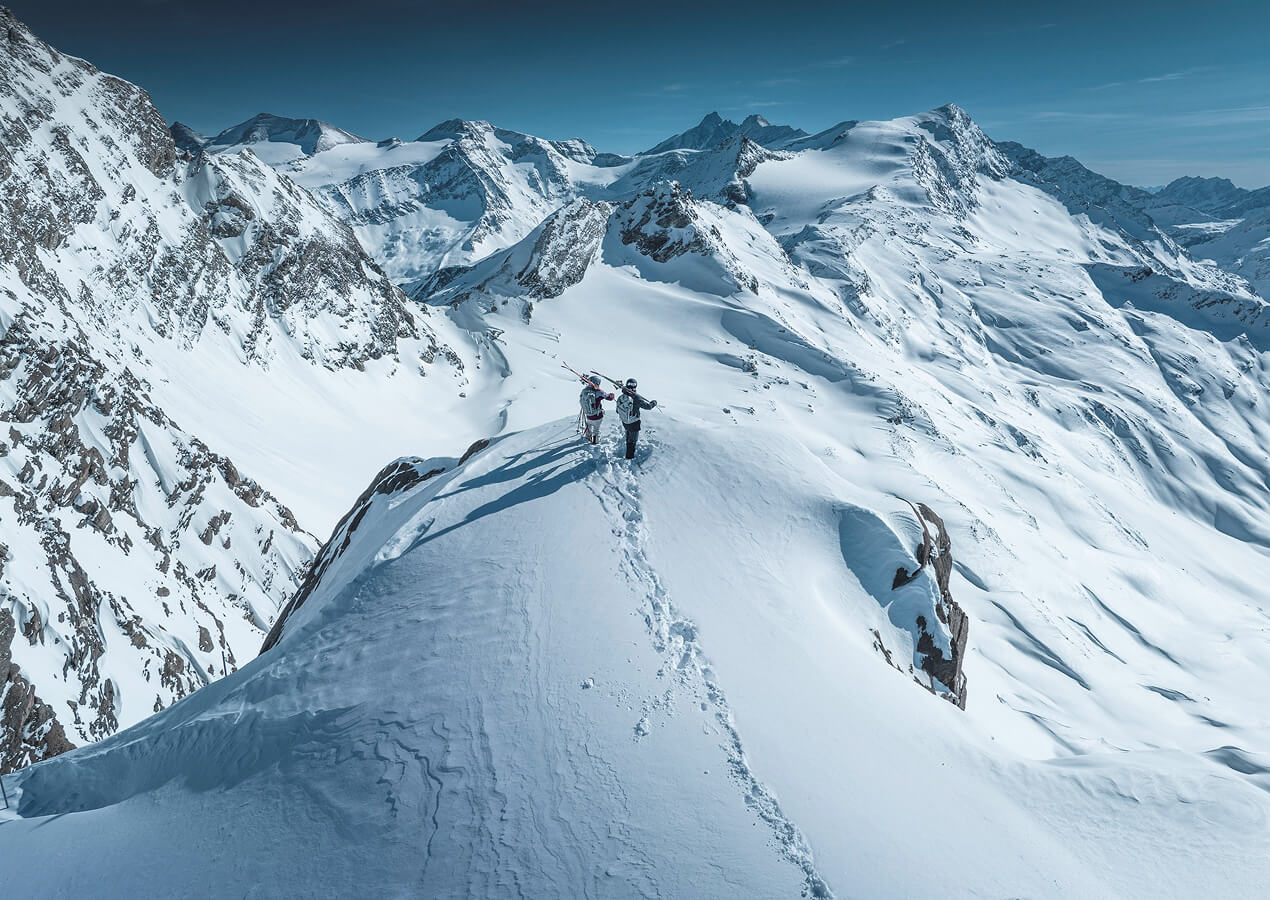Zwei Personen mit Ski stehen am Berggipfel